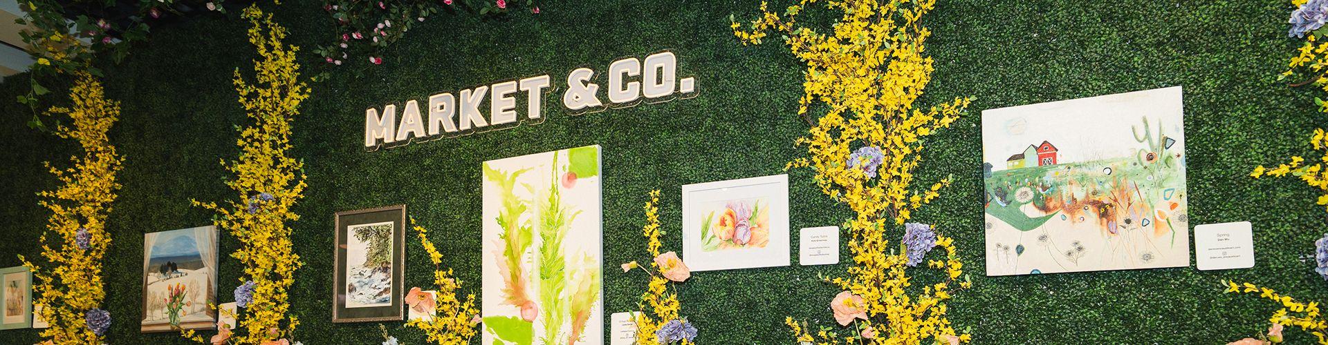 Floral Market & Co. art display on a green hedge wall with paintings