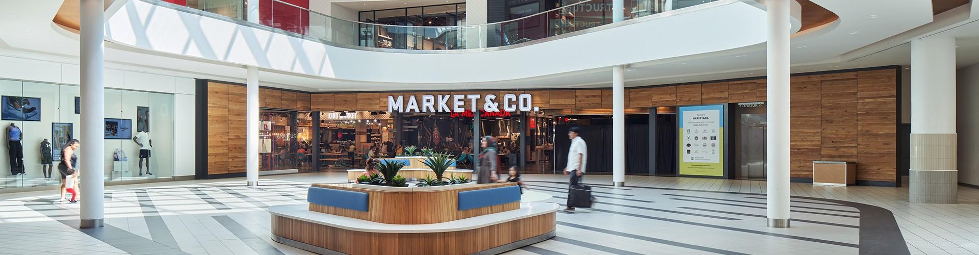 Mall atrium with a circular seating planter outside the Market & Co. food hall