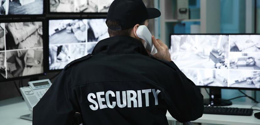 Security guard on the phone watching CCTV monitors in a control room