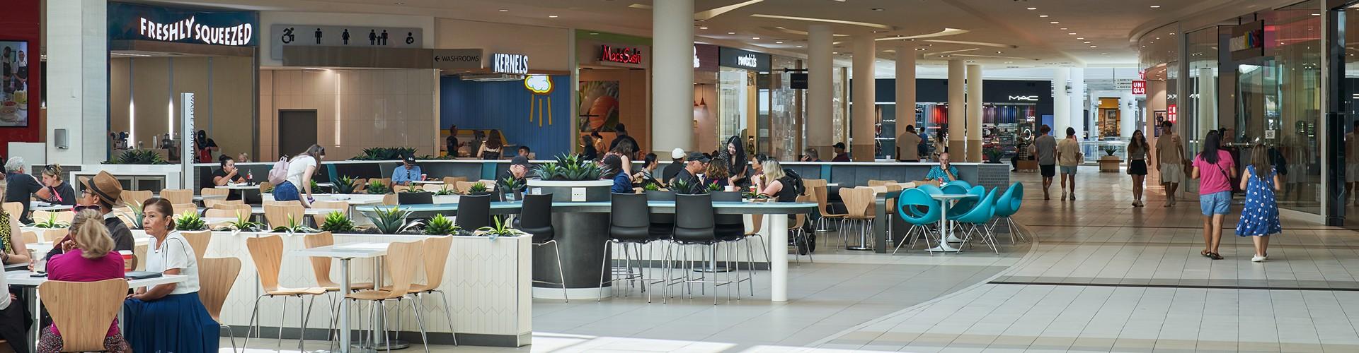 Mall food court with diners at tables near Freshly Squeezed and Kernels