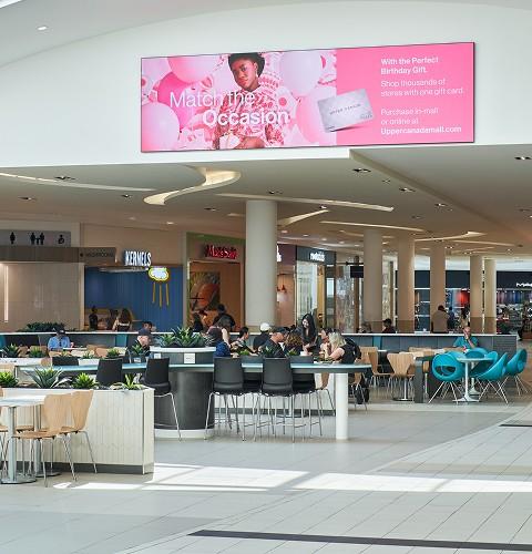 Mall food court with diners at tables near Freshly Squeezed and Kernels