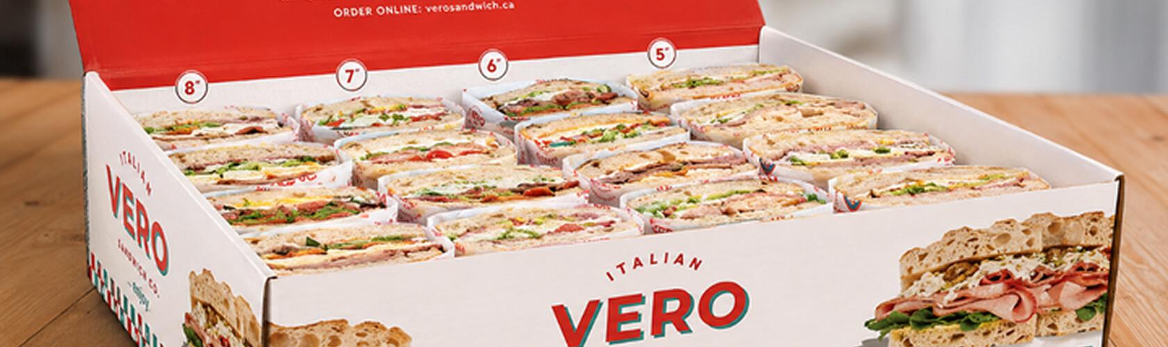 Open catering box of assorted Vero Italian sandwiches on a wooden table