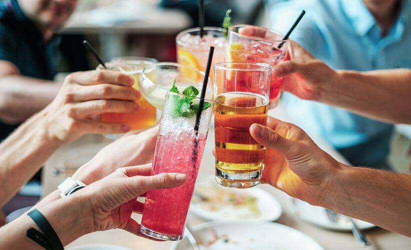 Group of friends clinking colourful cocktails together over a restaurant table