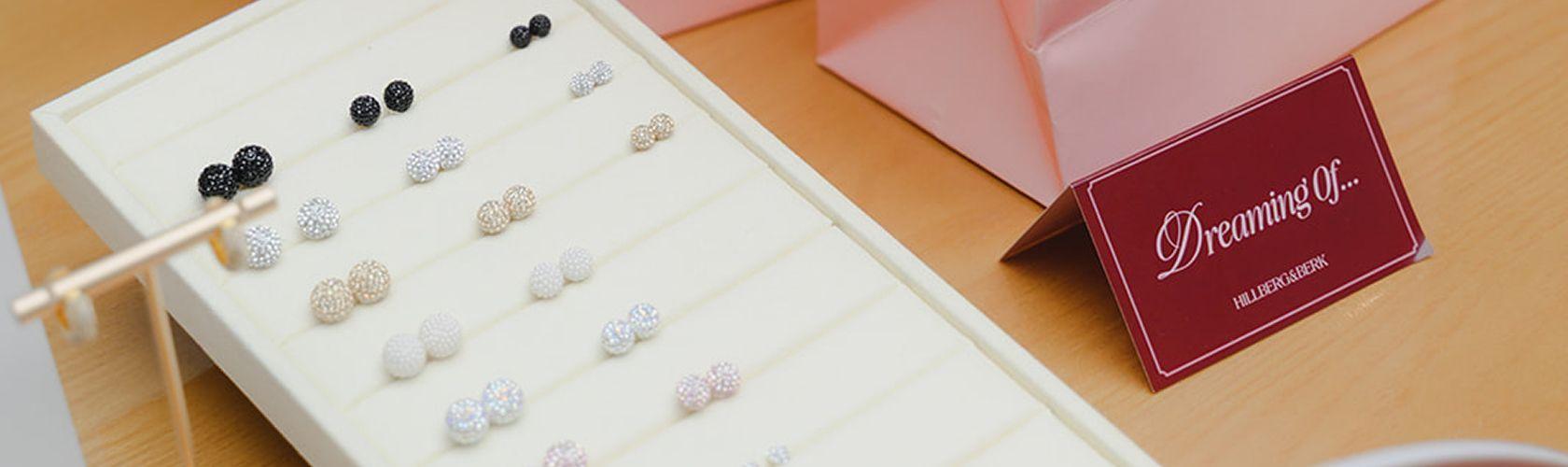 Tray of sparkly Hillberg & Berk stud earrings beside a Dreaming Of sign
