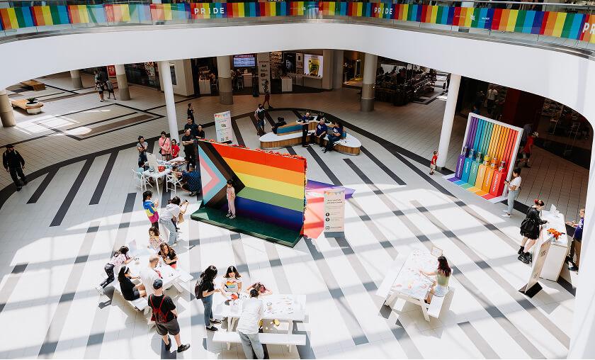 Pride celebration in the mall atrium with a large progress flag and visitors