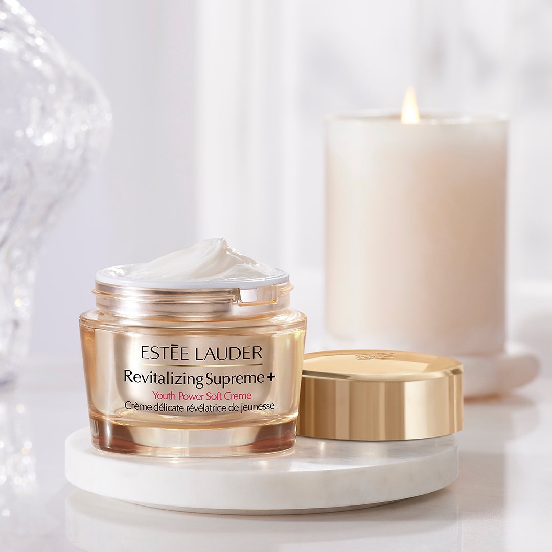 An Estee Lauder face cream is showcased on a white background alongside a white candle.