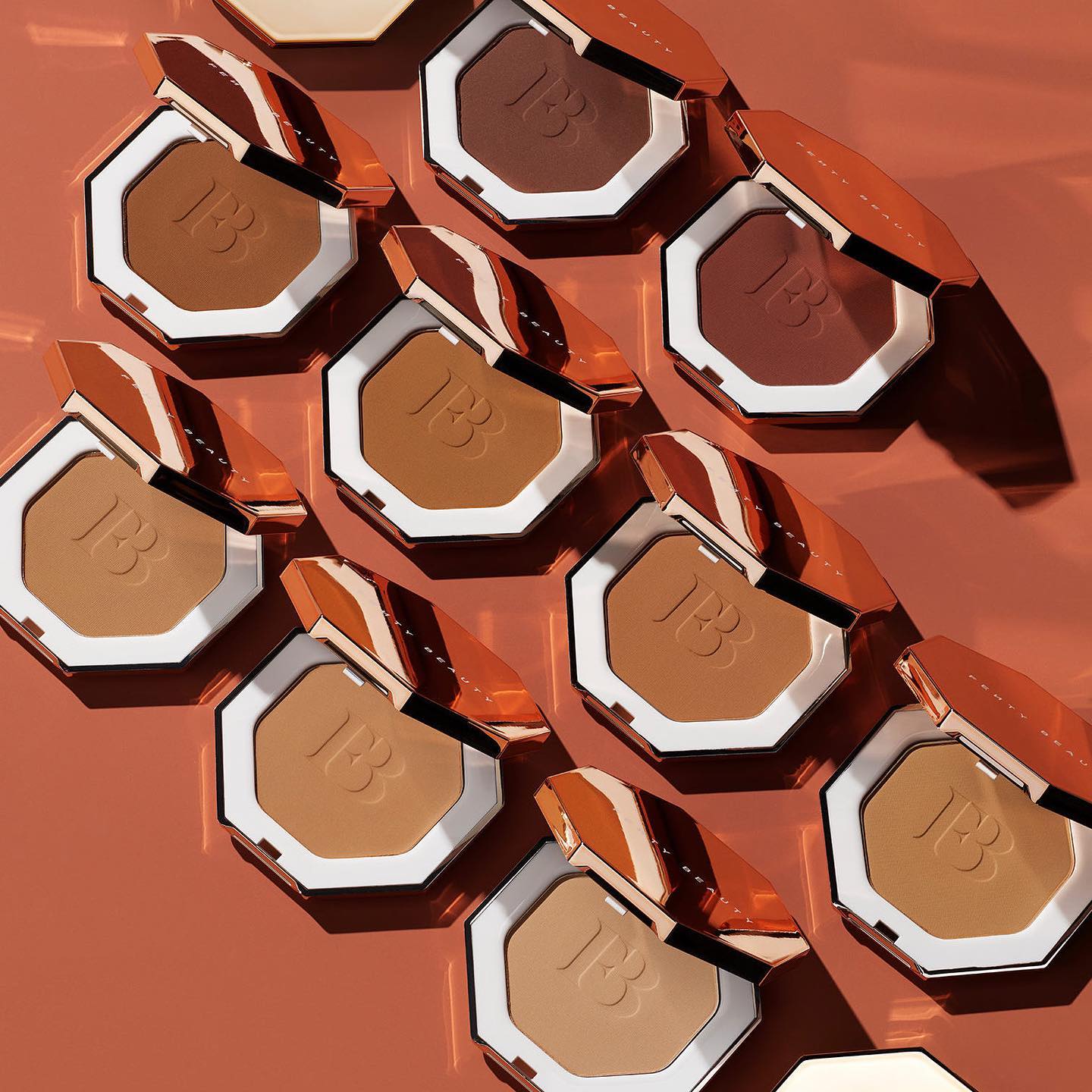 Various skin shades of Fenty Beauty bronzer are displayed on a rust orange background.