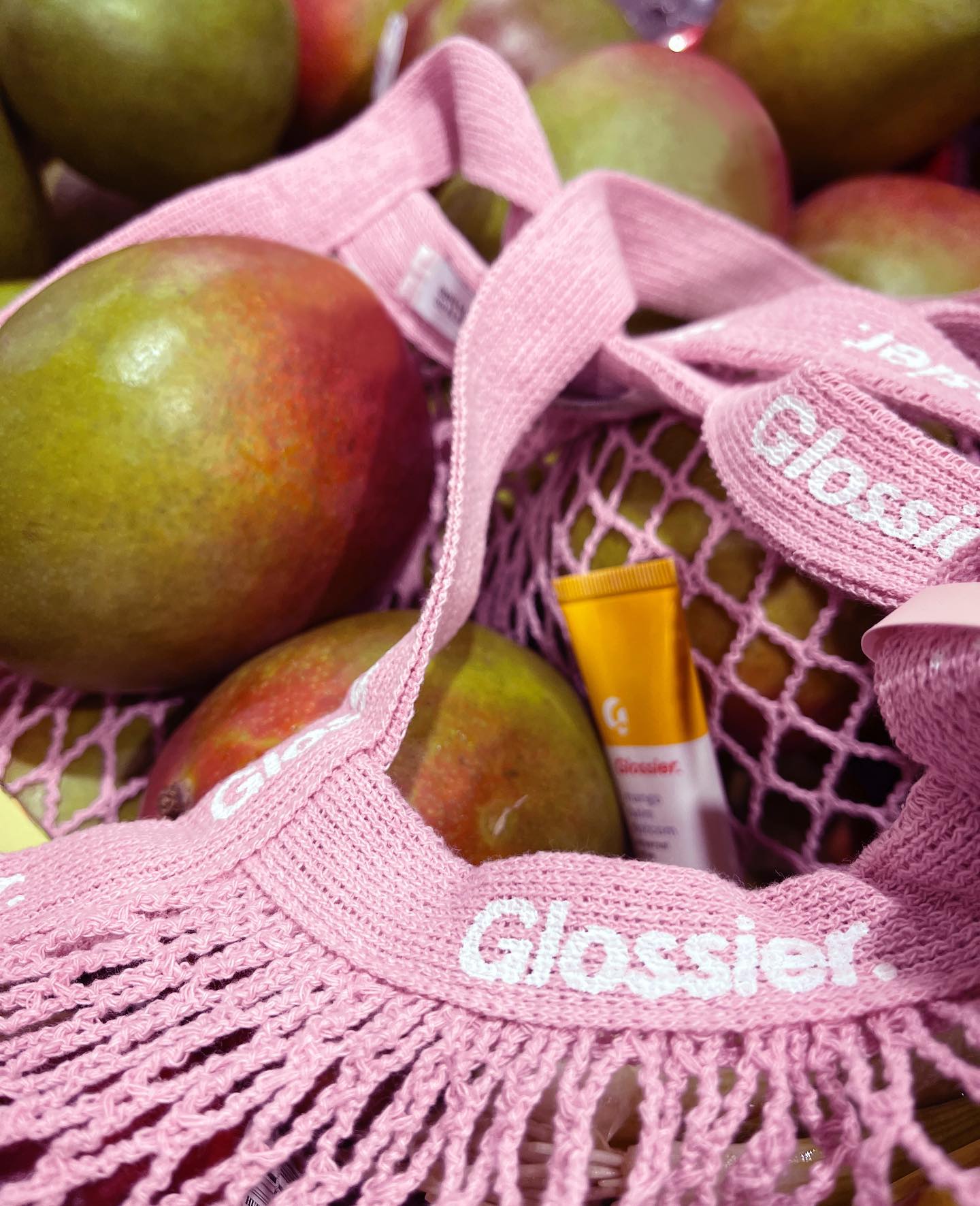Mangos and Glossier lip products are laid within a light pink Glossier fruit bag.