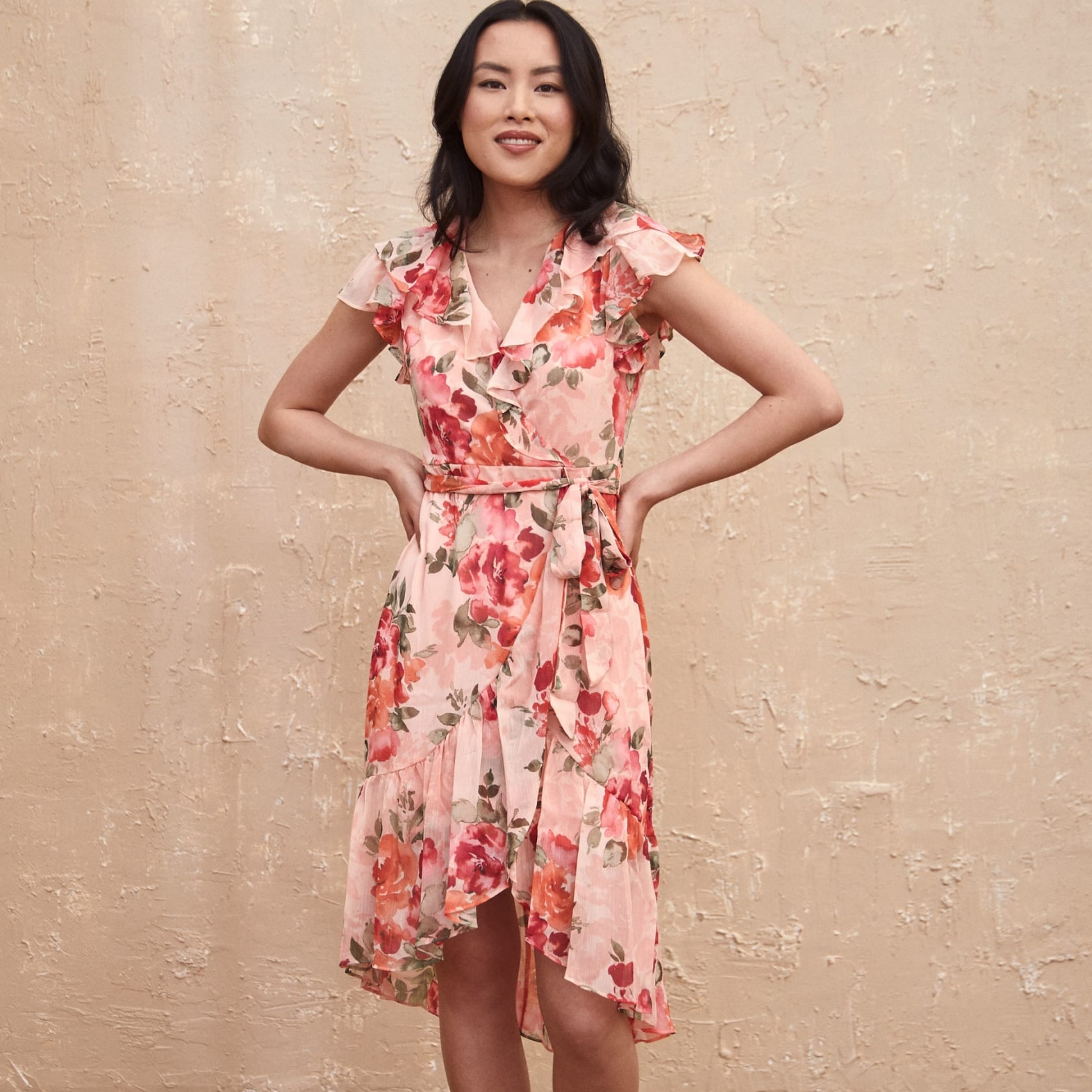 A dark haired woman poses in a light pink floral dress from Laura.