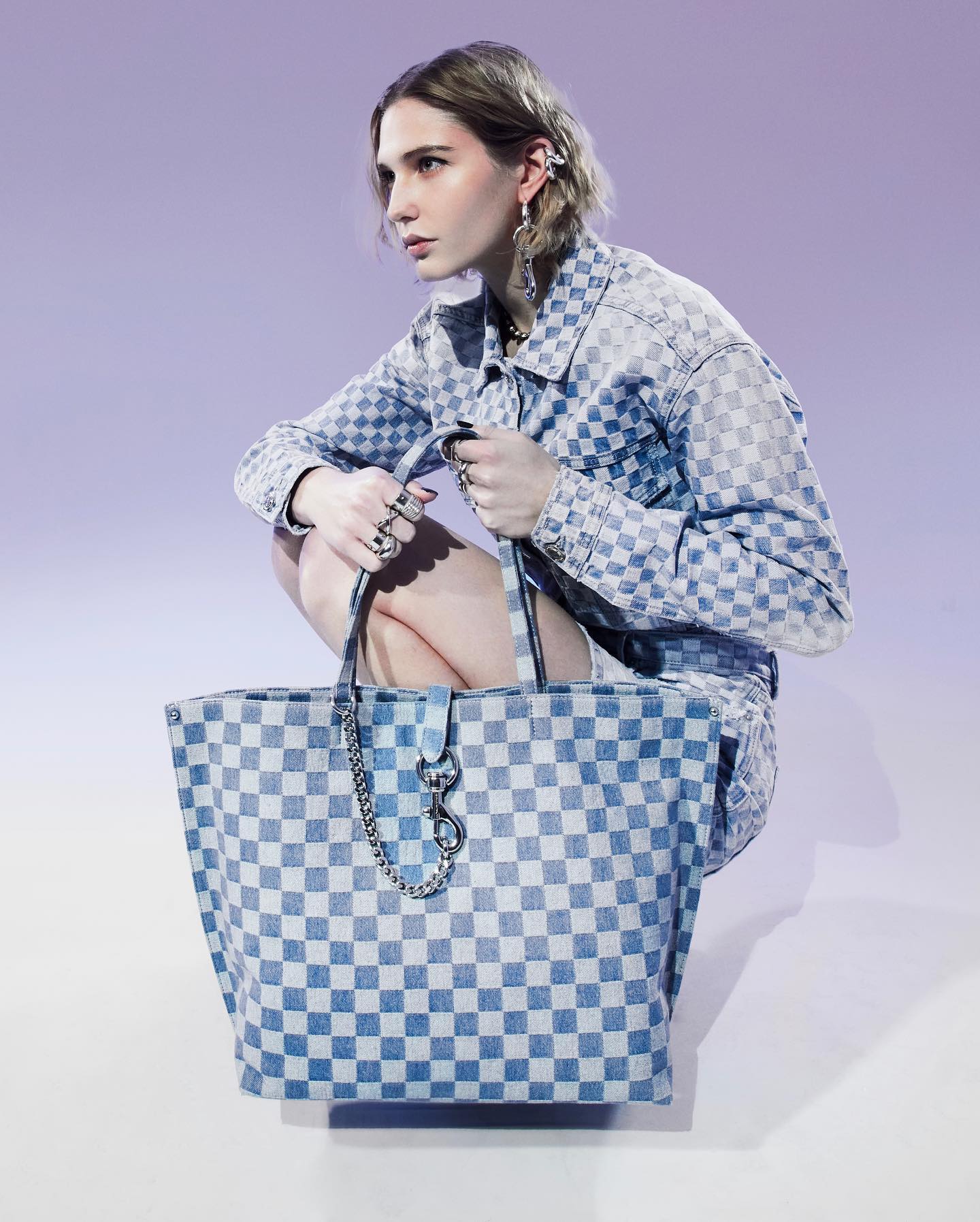 A woman bends at the knee while holding a blue checkered bag from Rebecca Minkoff. Her jacket matches the bag.