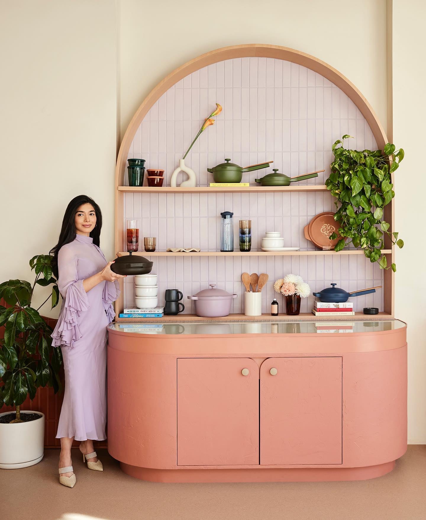 A woman holding an Our Place pan stands to the left of a retro inspired Our Place display.