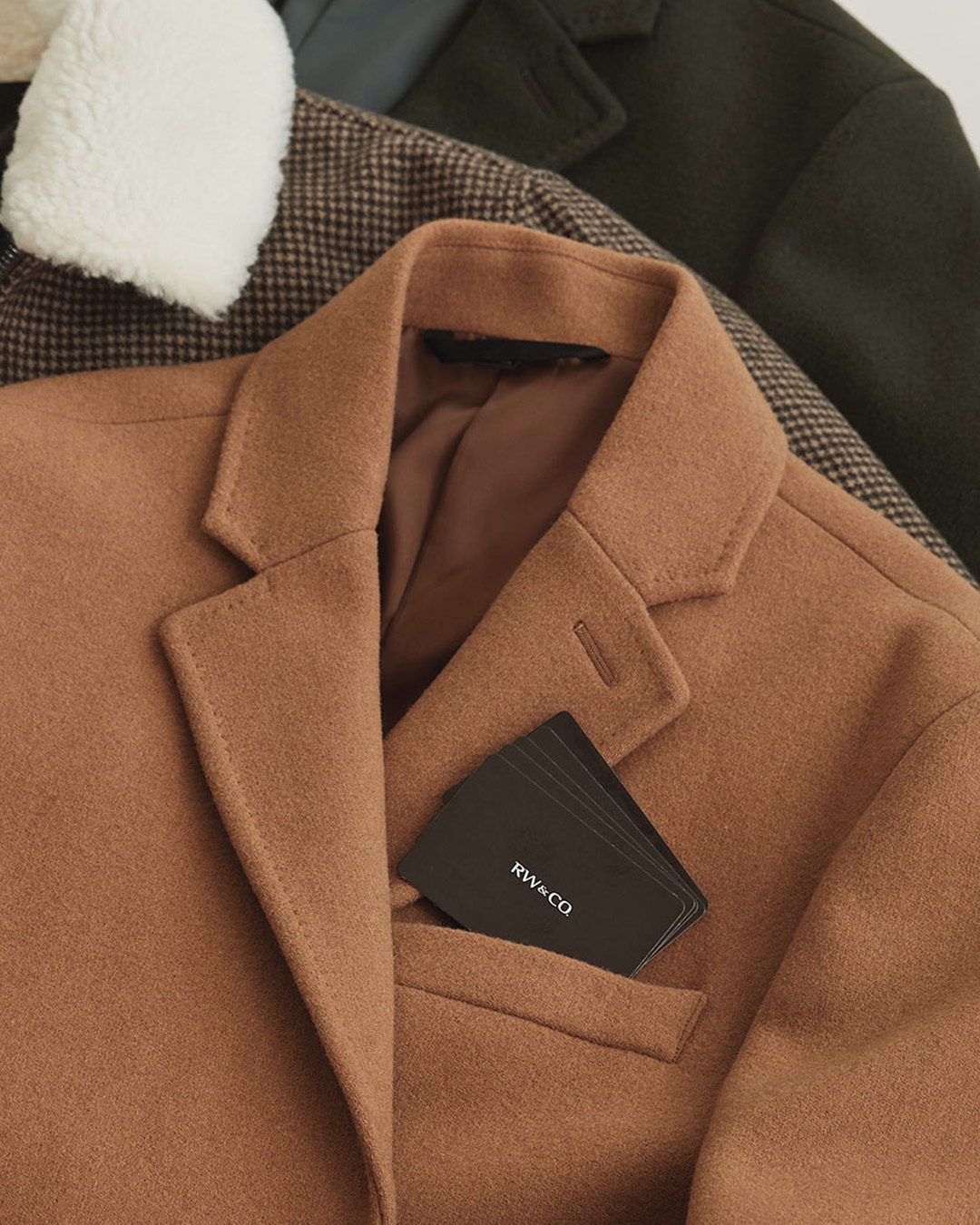 A tan coloured coat from RW&Co. is laid on top of other clothing.