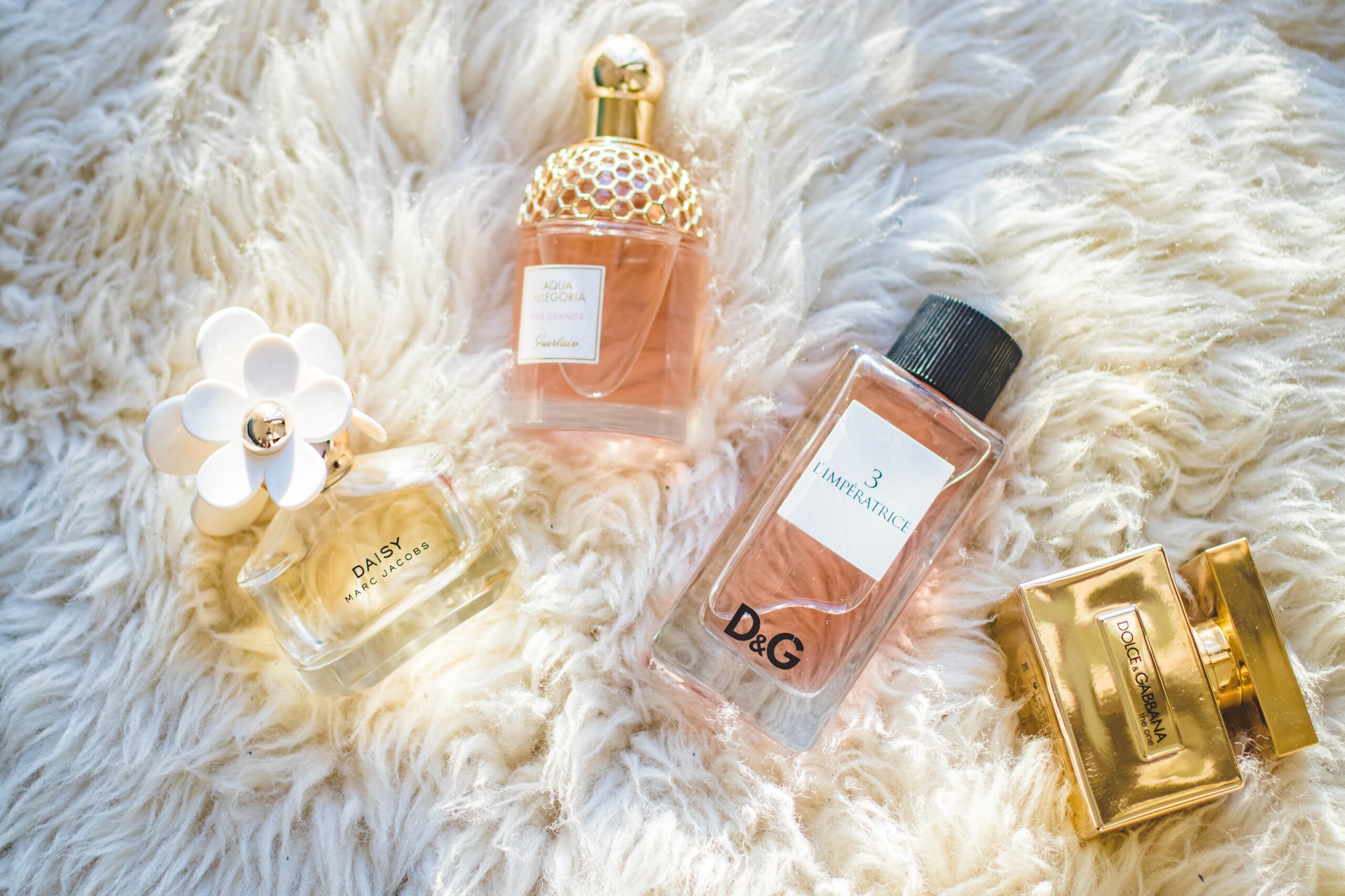 A variety of luxury perfumes lay on a fuzzy, white garment.