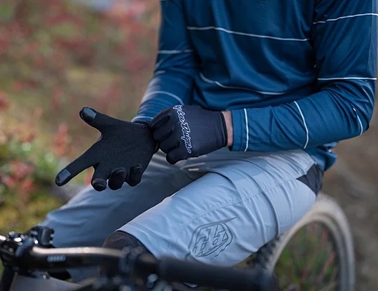 Close up image of a person on a bicycle putting on black cycling gloves.