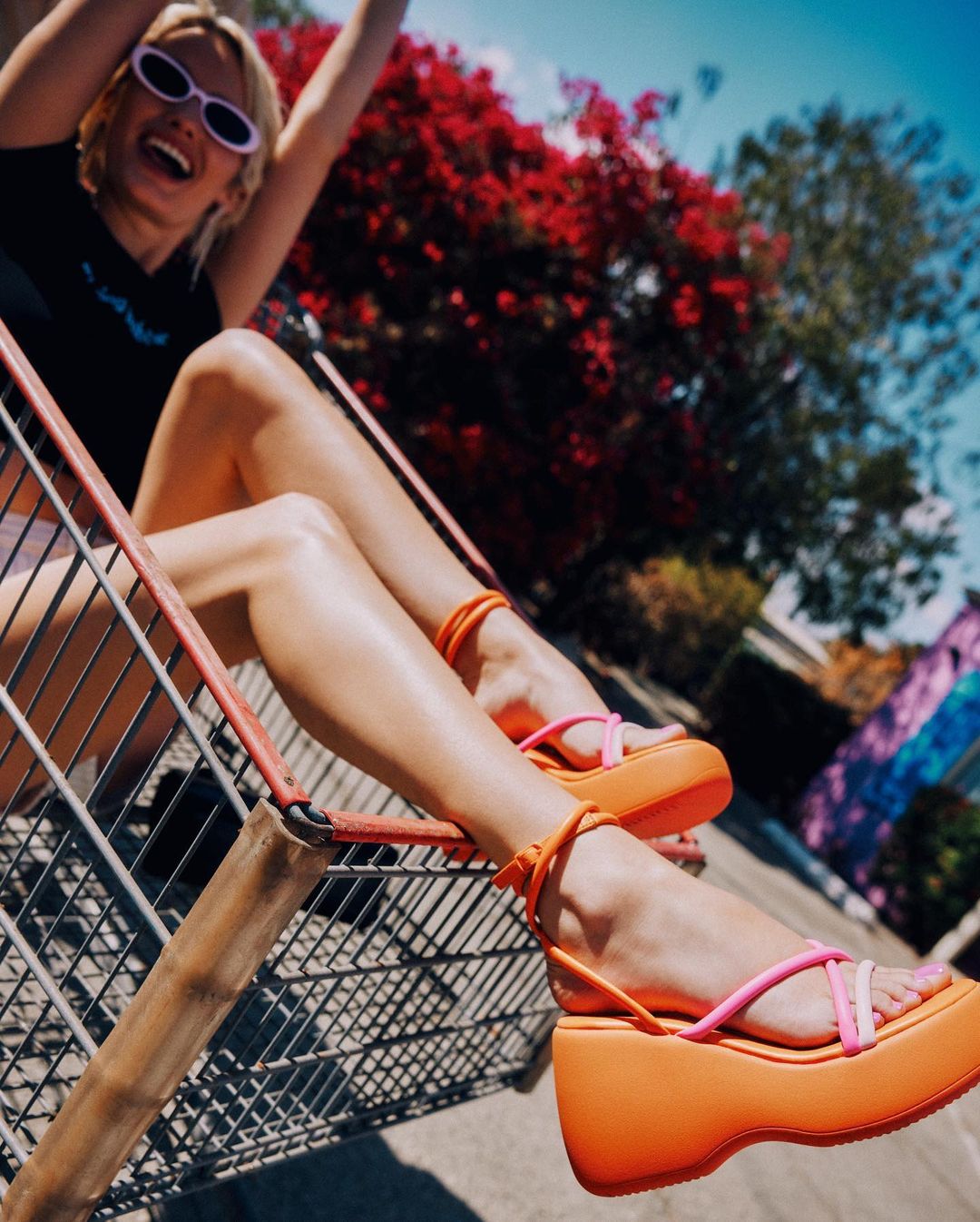 image of a woman sitting in a shopping cart showing off orange and pink wedge sandals