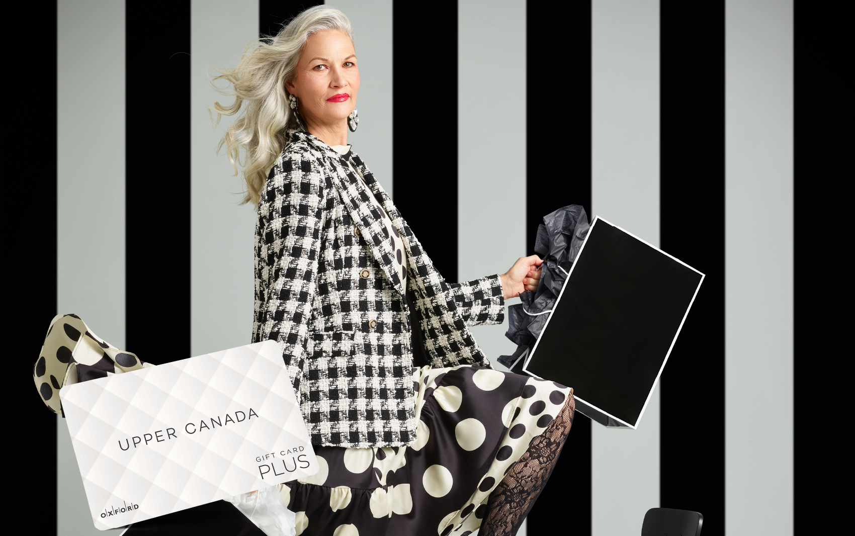 promotional image for a UCM gift card. It shows a woman wearing a black and white houndstooth blazer and black and white polka dot skirt holding black and white shopping bags. A UCM gift card is also in the image