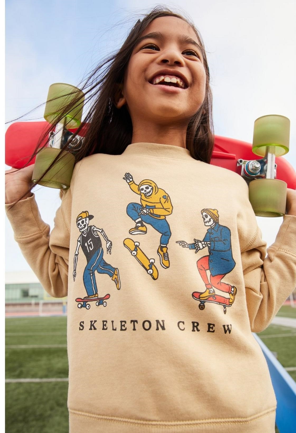image of a girl wearing a graphic sweatshirt and holding a skateboard behind her back