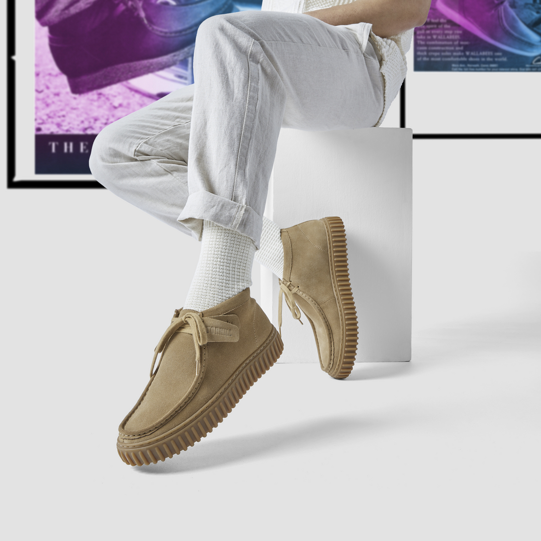 close-up of model sitting and wearing light wash jeans, white socks and tan clarks wallabee shoes