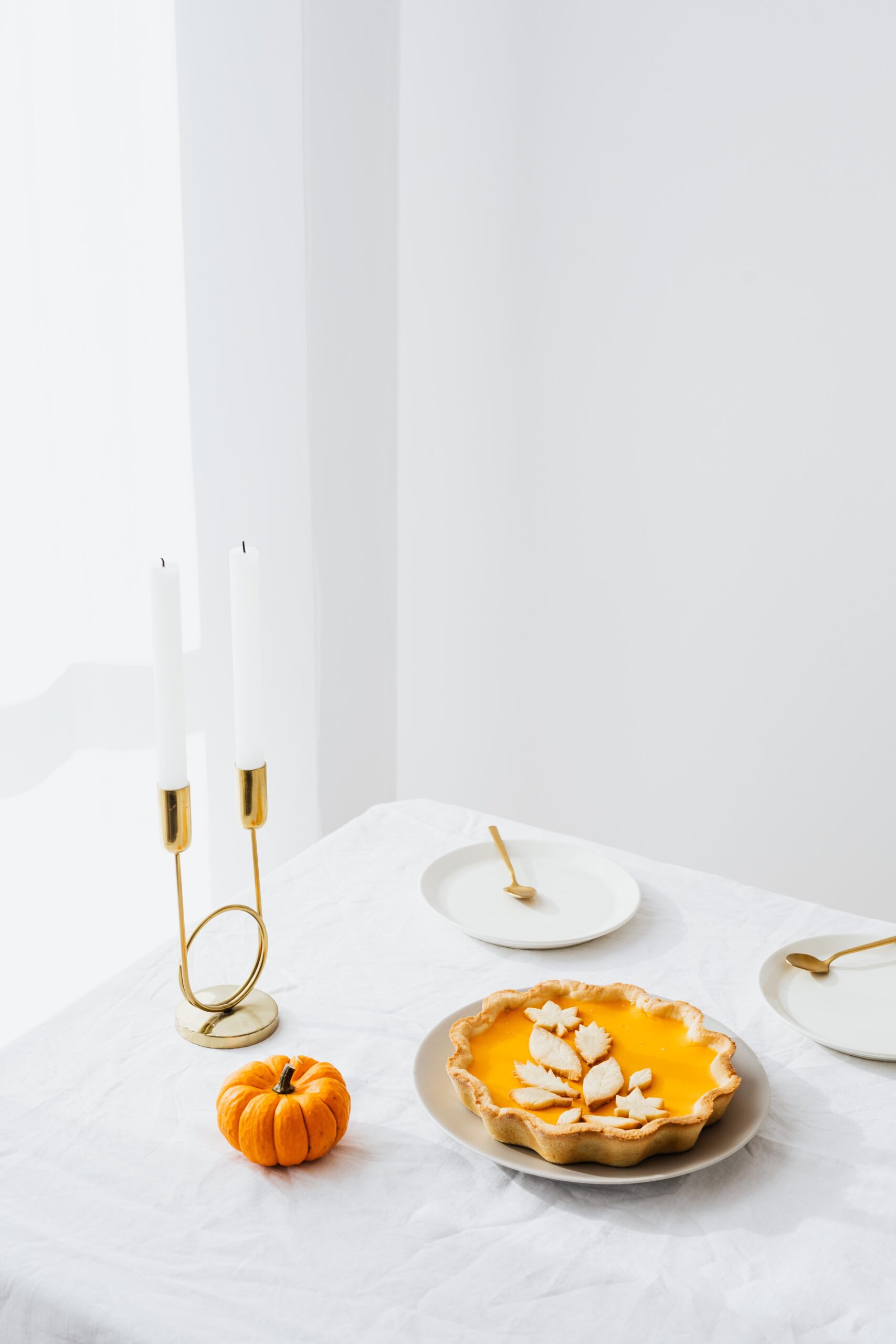 White tablecloth with candles, pumpkin pie, and a pumpkin set on top.
