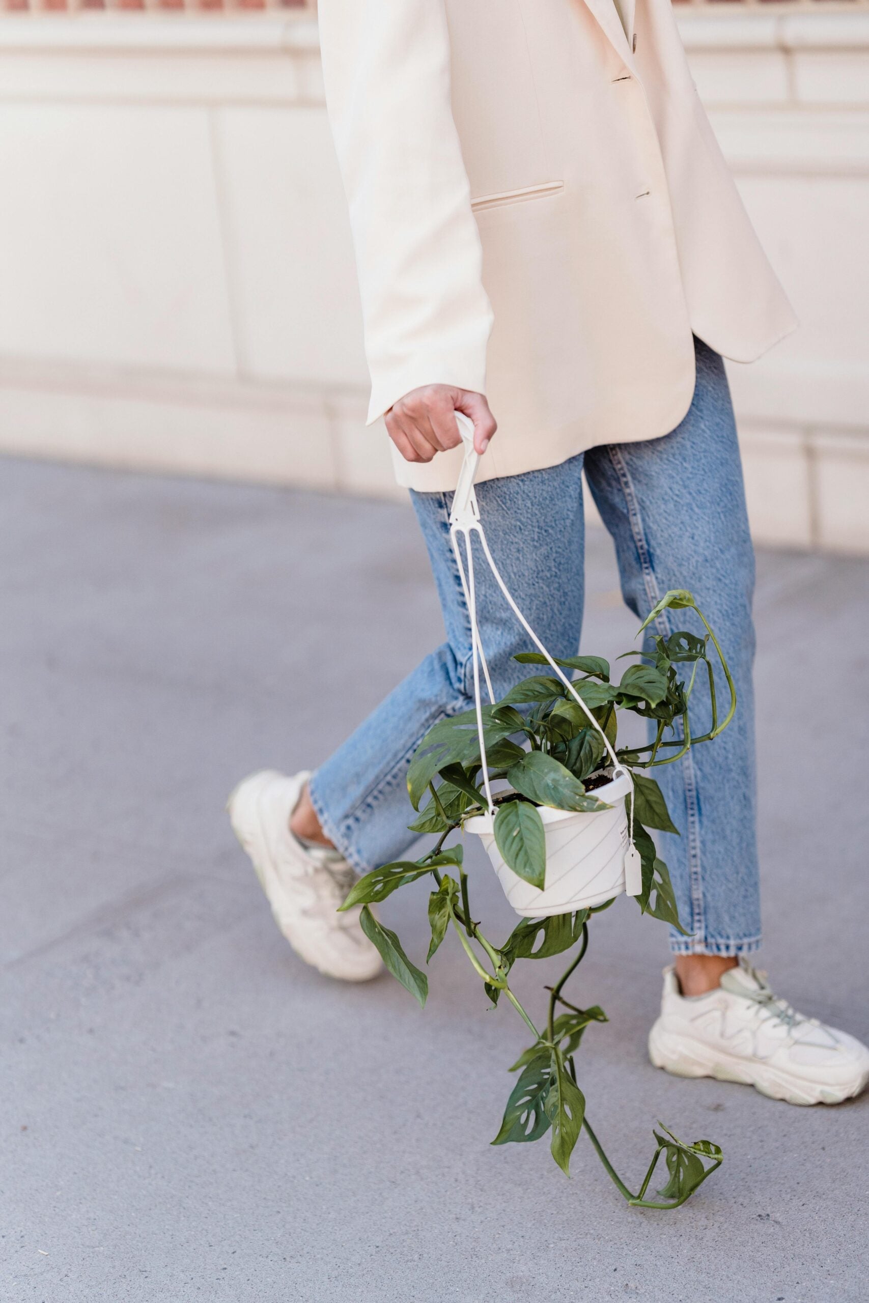 girl walking down the street in denim and cream blazer with a plant