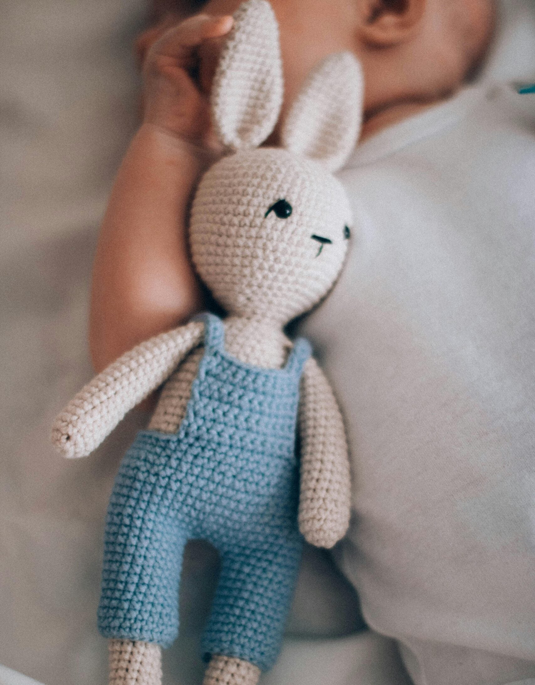 Stuffed rabbit in overalls beside a baby