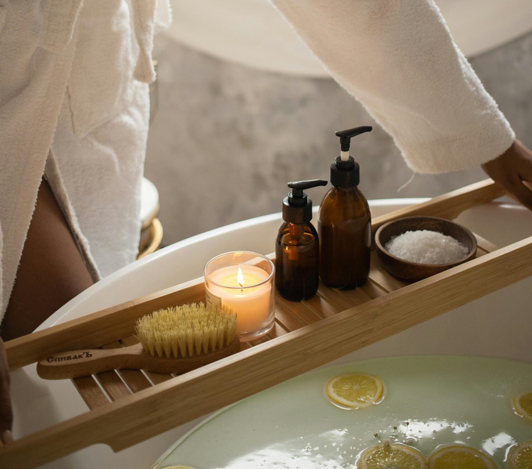 Person in a bathrobe setting up a bath with various bath items