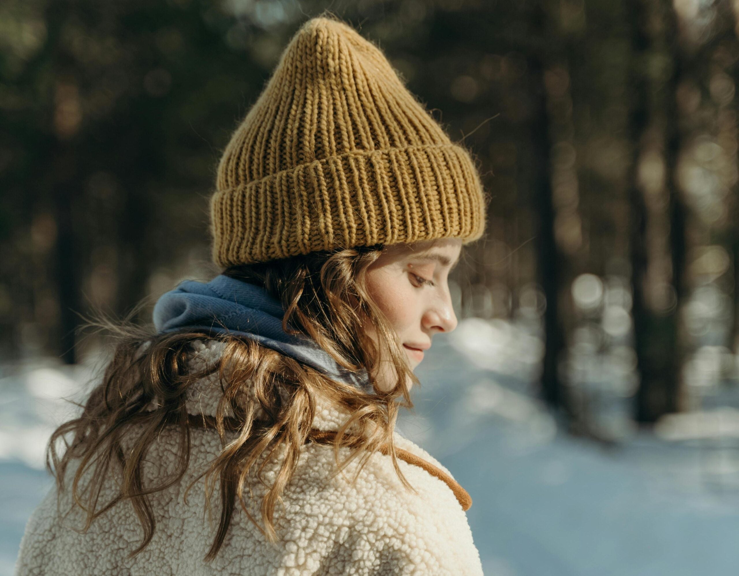 oman in the forest with a cream jacket, Blue Scarf and Brown Hat.